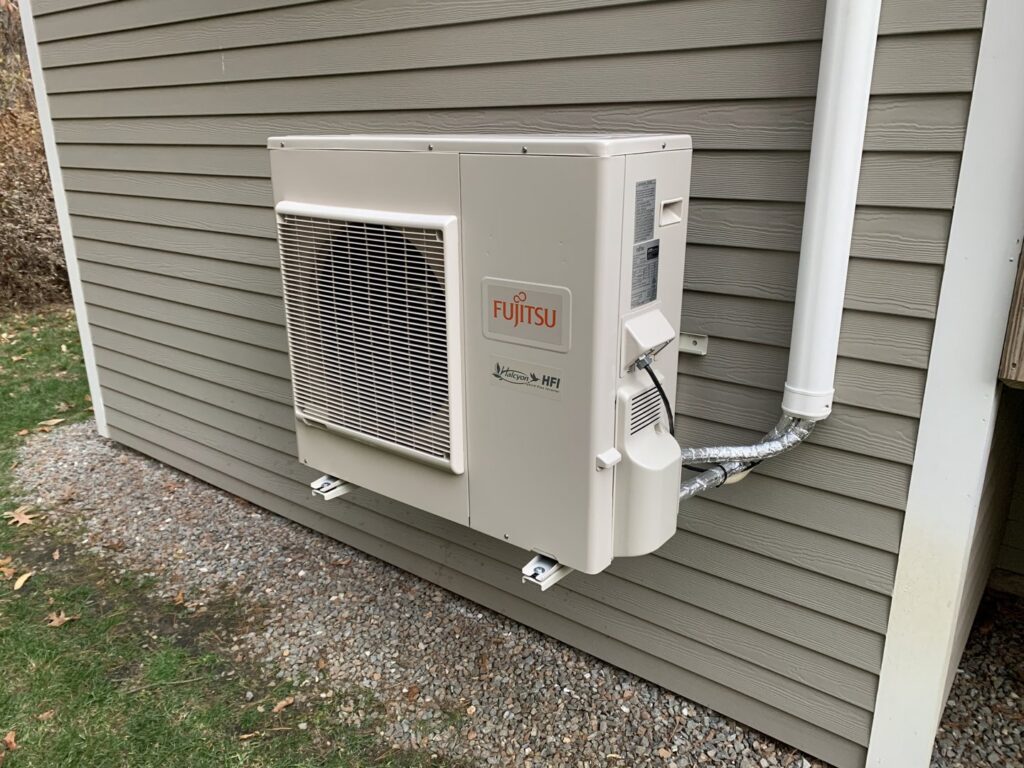 An outdoor Fujitsu HFI mini-split condenser unit installed on the side of a house by Elite Heating and Cooling in Livonia, MI.