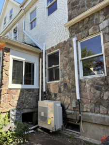 A Fujitsu mini-split outdoor condenser unit installed on the side of a stone house by Fast Air in Zebulon, NC