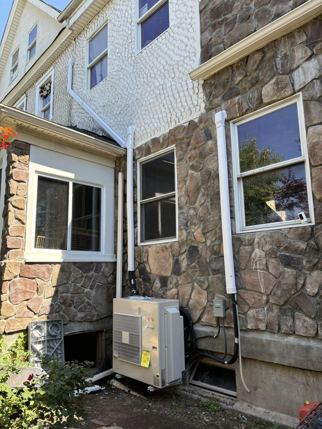 A Fujitsu mini-split outdoor condenser unit installed on the side of a stone house by Fast Air in Zebulon, NC