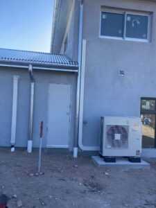 An outdoor Fujitsu mini-split condenser unit installed next to a new construction building by Santa Fe Heating & Cooling LLC in Santa Fe, NM.