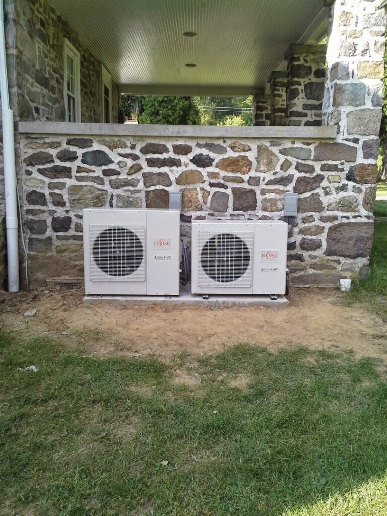 Two Fujitsu mini-split outdoor HVAC units installed next to a stone wall by Capitol Heating and Air in Morgantown, PA.