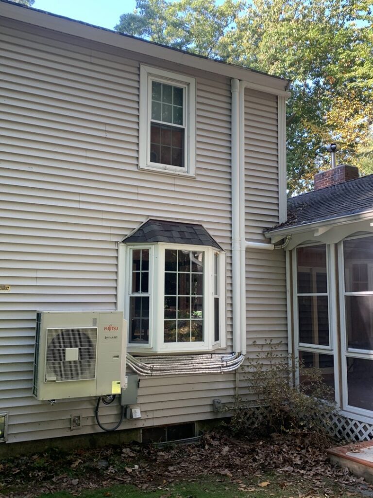 A Fujitsu mini-split outdoor condenser unit mounted on the side of a house by Elite Mechanical in Manchester, NH.
