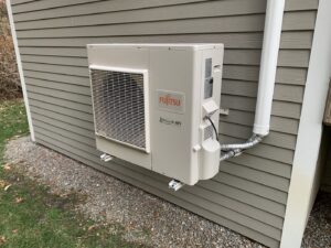 A Fujitsu outdoor mini-split condenser unit mounted on a home's exterior by Elite Mechanical in Manchester, NH.