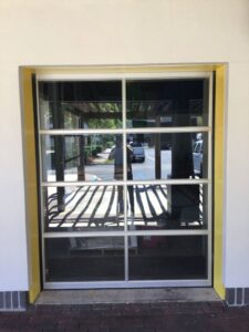 A modern full-view glass garage door with a distinctive yellow frame installed by Magic City Door Huntsville in Birmingham, AL.