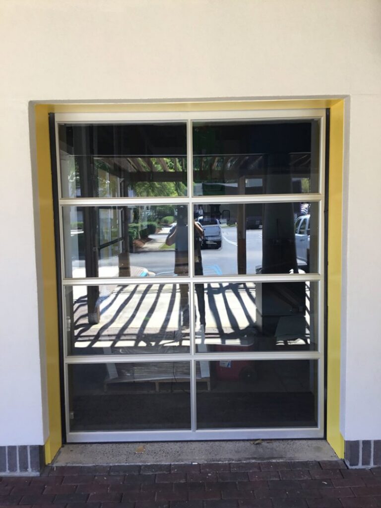 A modern full-view glass garage door with a distinctive yellow frame installed by Magic City Door Huntsville in Birmingham, AL.