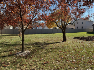 A full view of a tan vinyl fence project enclosing a large residential property, installed by H&M Fencing LLC in Decatur, IN.