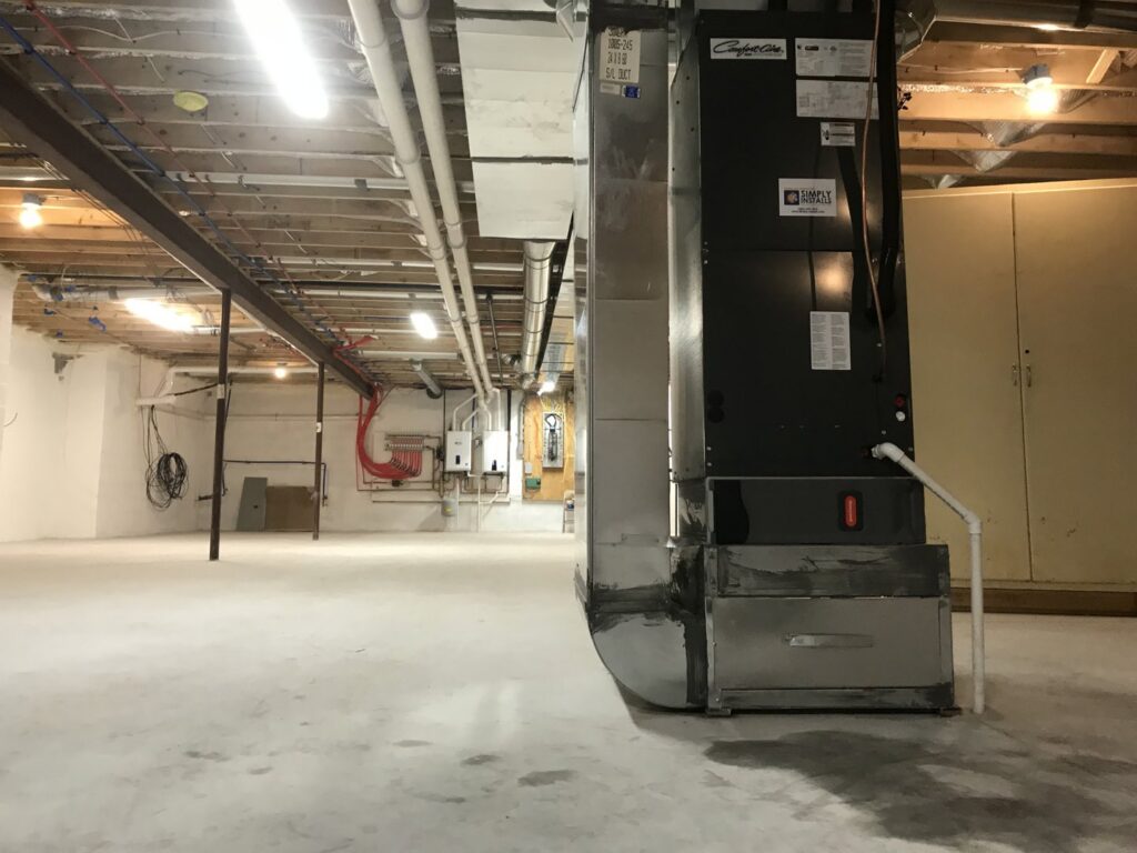 A large furnace or air handler unit installed in a spacious basement by Simply Installs Heating & Air Conditioning in Shortsville, NY.