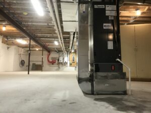 A large furnace or air handler unit installed in a spacious basement by Simply Installs Heating & Air Conditioning in Shortsville, NY.