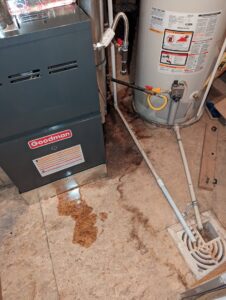An indoor furnace and water heater with a visible leak on the floor, indicating a service need for Fix It Now Heating and Cooling in Thornton, CO