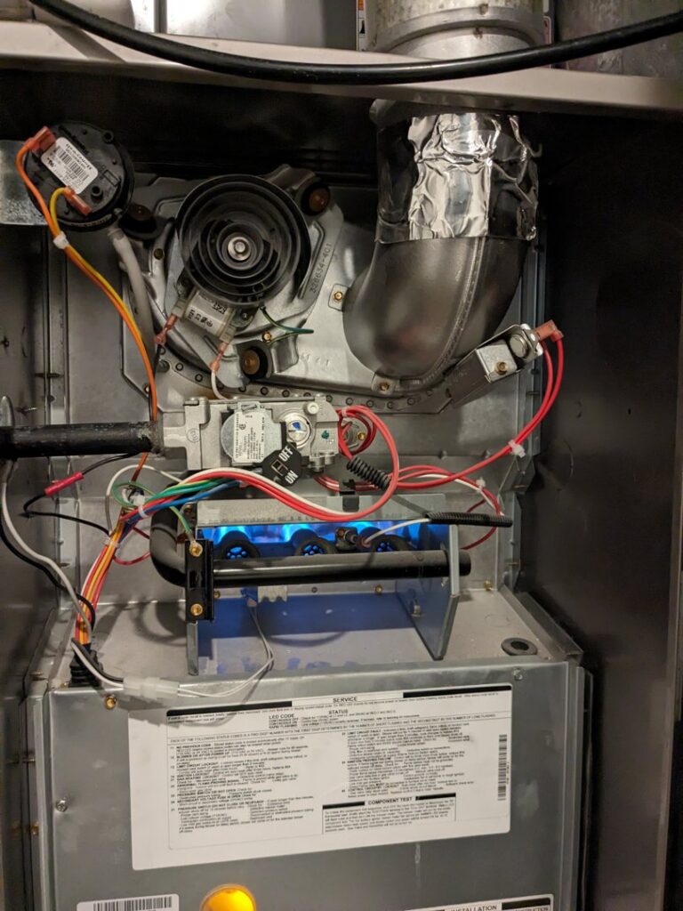 A close-up view of a furnace burner with a blue flame during an inspection by Inspector Rogers LLC in Draper, UT.