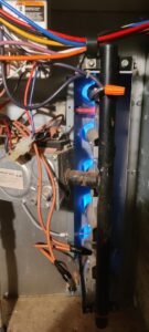 Close-up of furnace burners with blue flames, indicating a heating system check or repair by Brady Air & Home Repair LLC in Asheboro, NC.