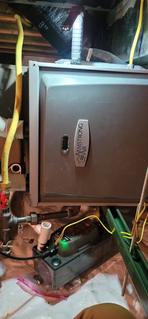 Close-up of an Armstrong Air furnace with a condensate pump and piping, indicating HVAC service by Northern Peak Heating & Cooling in Bozeman, MT.
