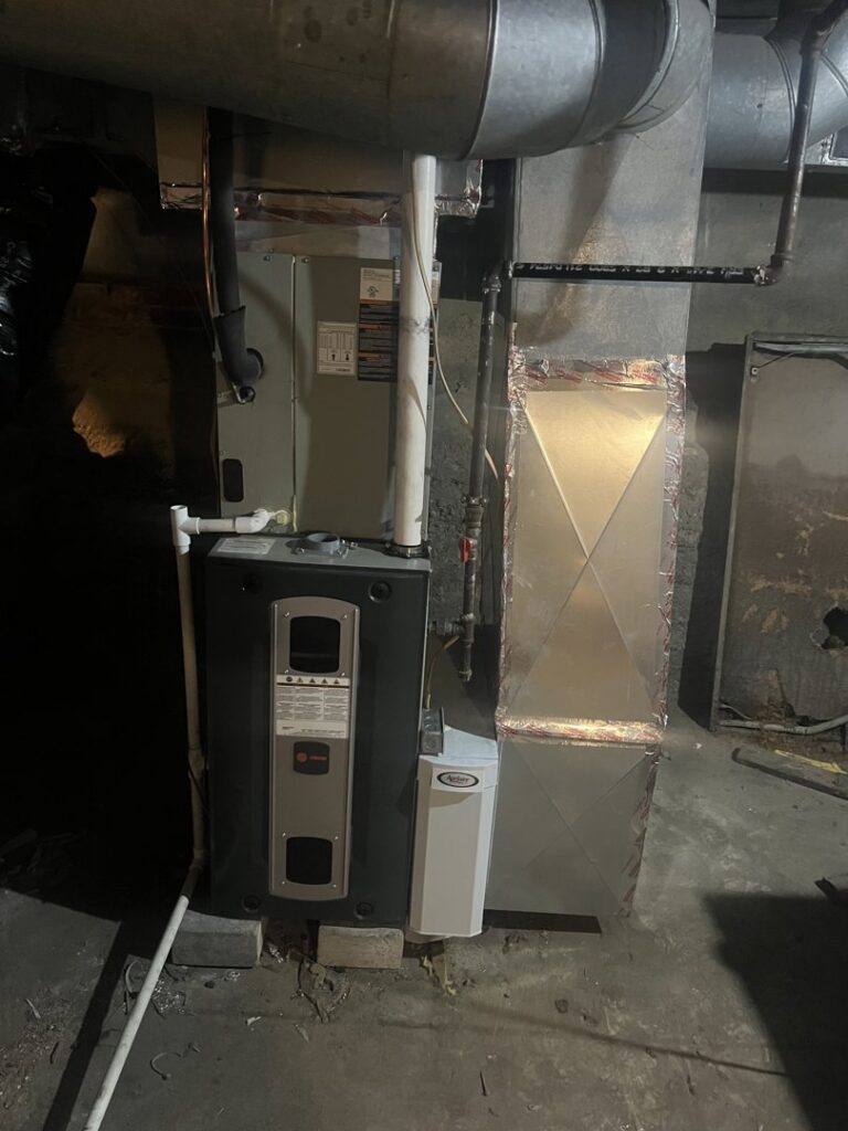 A furnace and air handler unit with an attached humidifier in a basement by Breezy Brothers Heating and Cooling in Lafayette, IN.