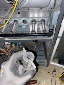 A technician holding a furnace igniter during a repair or replacement by Infinite Heating & Air in Newnan, GA.