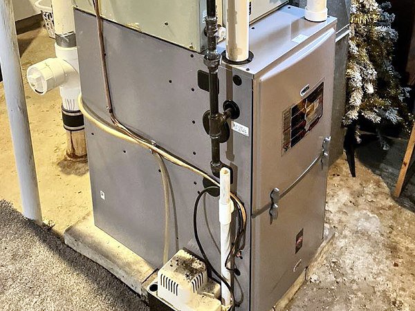 A furnace unit with piping and wiring, indicating installation or service by QC Mechanical, Inc. in Lockport, NY.