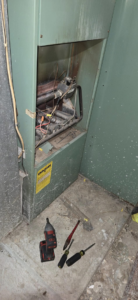 An older furnace with its access panel open and tools on the floor, showing repair work by McBride HVAC Solutions LLC in Cincinnati, OH