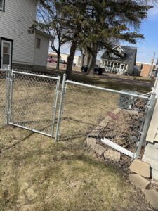 A galvanized chain-link fence with a gate next to a residential house, installed by Mauer Company in Little Canada, MN.