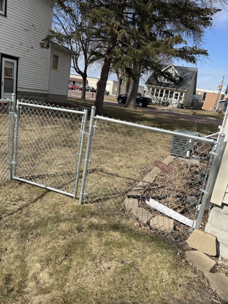 A galvanized chain-link fence with a gate next to a residential house, installed by Mauer Company in Little Canada, MN.