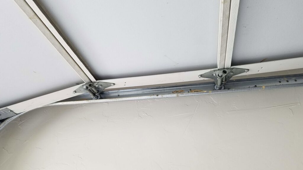 A close-up view of garage door hinges and tracks from the interior, showing repair work by Johns Garage Doors in Tucson, AZ.
