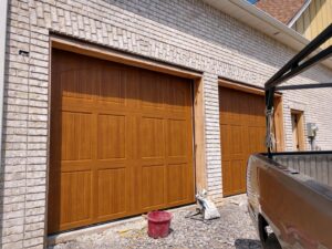 Garage door installation in progress with brown wood-look doors and a service truck nearby by Ken's Overhead Door in Clarksville, TN.