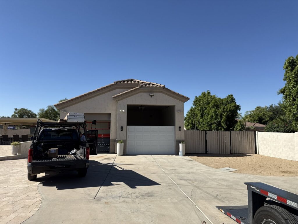 An exterior view of a house with a garage door installation in progress, with a service truck and lift from MGG Garage Door Service in San Tan Valley, AZ