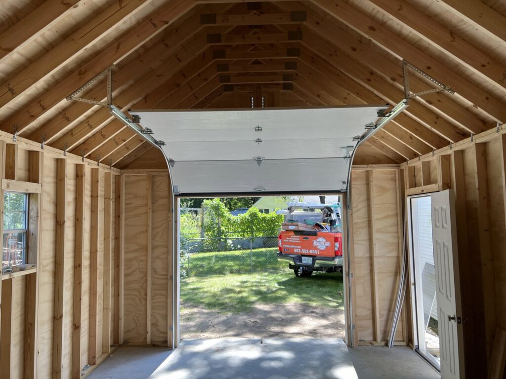 Interior view of a garage showing a white garage door installation in progress by PM Garage Door in Hudson, NH.