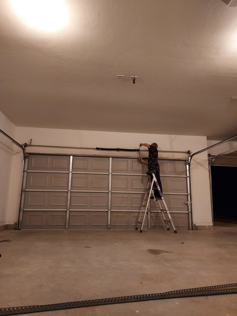A worker on a ladder performing garage door installation or repair for Zee's Garage Doors in Oklahoma City, OK.