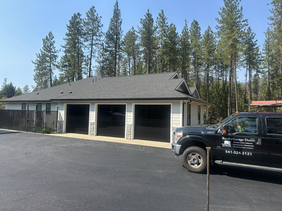 A Reed's Garage Door Systems LLC service truck parked outside a home with newly installed black garage doors in Sutherlin, OR.