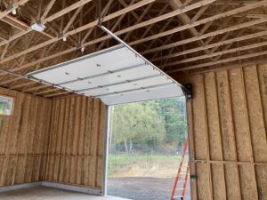 Interior view of a garage showing a white garage door partially open with tracks and opener installed by Independent Garage Doors LLC in Tacoma, WA.