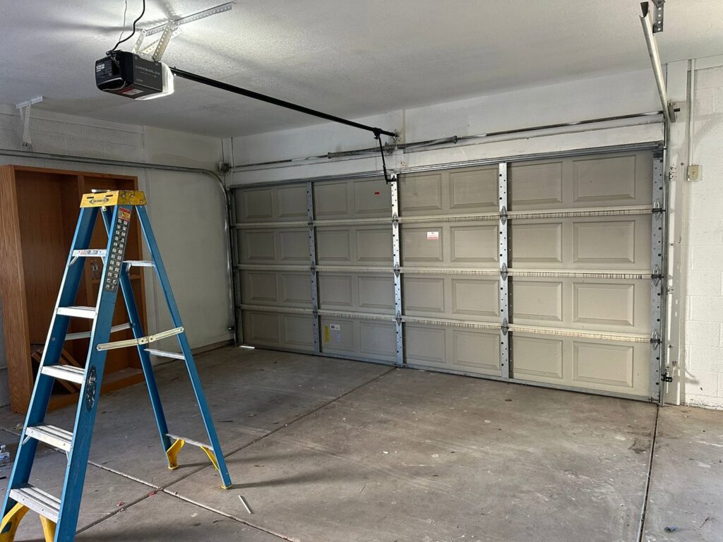Interior view of a garage showing an installed garage door, opener, and a ladder, indicating recent work by Central Garage Door Repair LLC in Glendale, AZ.