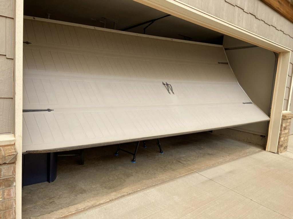 A garage door that is off its tracks and partially collapsed, needing repair from Unhinged Garage Doors LLC in Oklahoma City, OK.