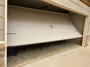 A garage door that is off its tracks and partially collapsed, needing repair from Unhinged Garage Doors LLC in Oklahoma City, OK.