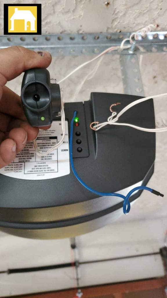 Hand holding a garage door opener safety sensor, indicating repair or installation work by TH Locksmith And Garage Door Repair, Vancouver, WA.