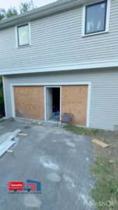 A garage door opening temporarily boarded up with plywood, indicating a repair or new installation project by QuickFix Garage Door Service in Brighton, MA.