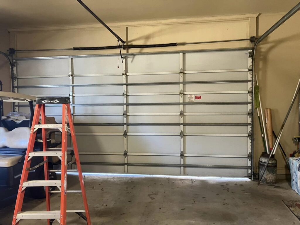 An interior view of a garage showing a white garage door with springs and tracks, indicating a repair or installation in progress by Superior Garage Door & Repairs in Lafayette, LA.