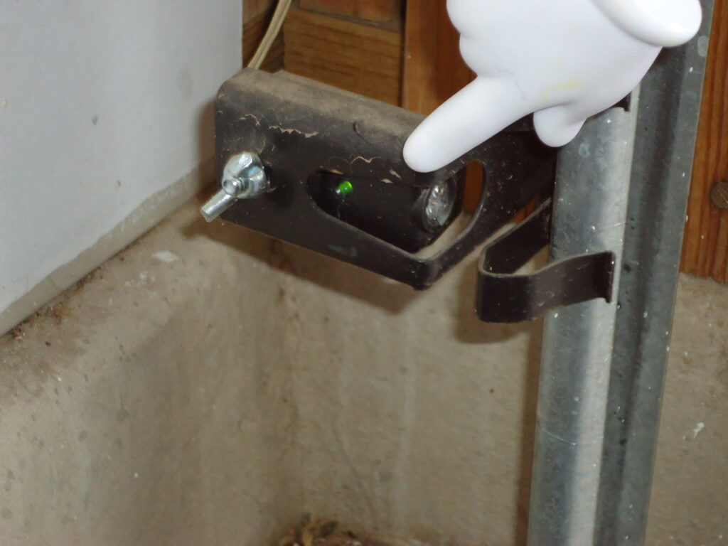 A close-up of a garage door safety sensor with a green light, indicating a check or installation by Able Garage Door Service, LLC in Tucson, AZ.