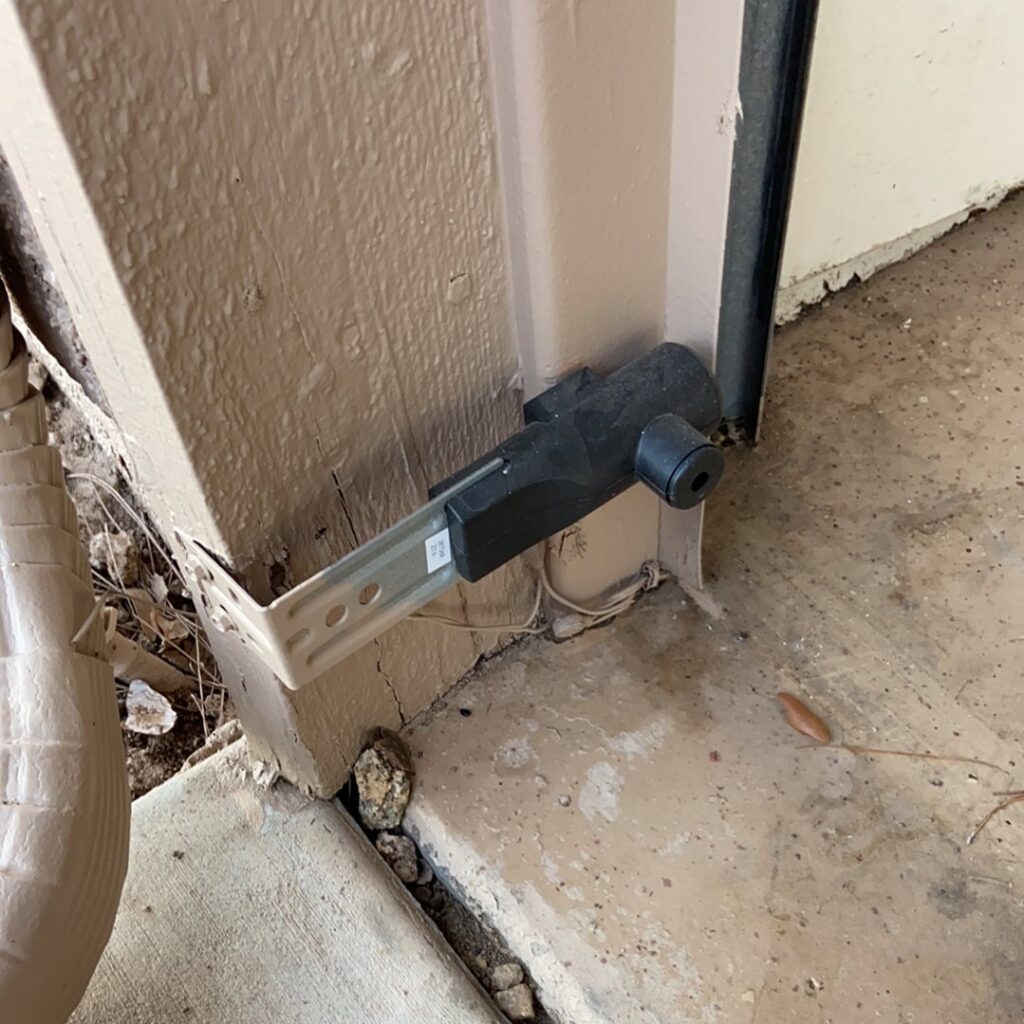 A close-up of a garage door safety sensor installed near the bottom of the door frame by MGG Garage Door Service in San Tan Valley, AZ