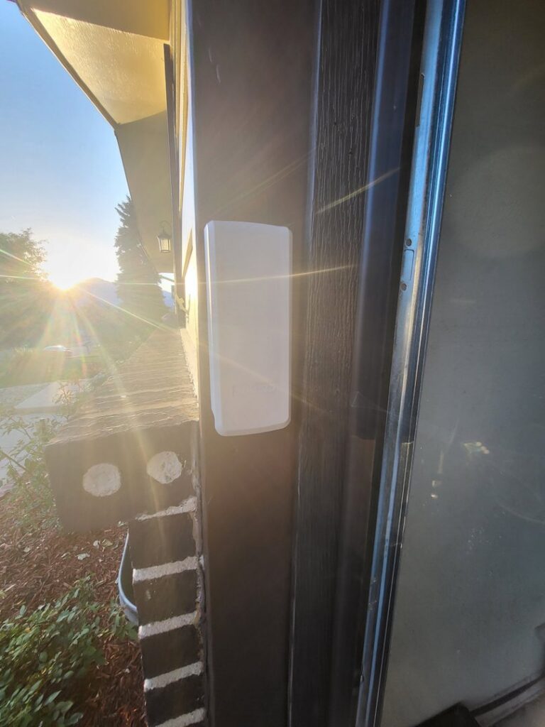 A white garage door sensor or control unit installed on a wall, part of a system by Mountain Fox Garage Doors in Colorado Springs, CO.