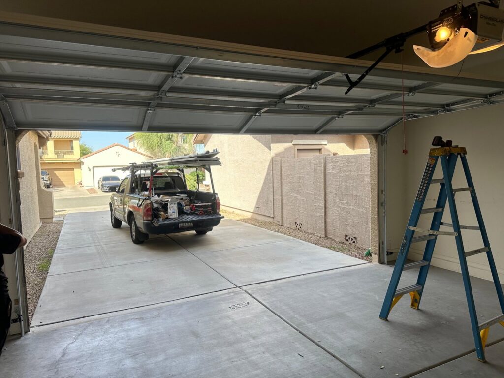 Garage door service in progress with a Central Garage Door Repair LLC truck and ladder inside a residential garage in Glendale, AZ.