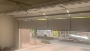 A Fix It Now Garage Doors.com service truck and trailer parked outside a garage with the door partially open in Tempe, AZ.