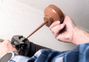 A technician lubricating a garage door spring mechanism during maintenance by Overhead Door of New Orleans in New Orleans, LA.