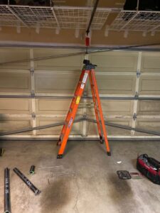 A ladder set up for garage door spring replacement, with new springs and tools on the floor by BSD Garage Door Service in Naperville, IL.
