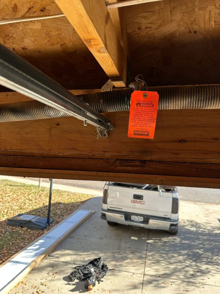 Close-up of garage door springs with a warning tag, indicating repair or maintenance by Strongdoor garage in Denver, CO.