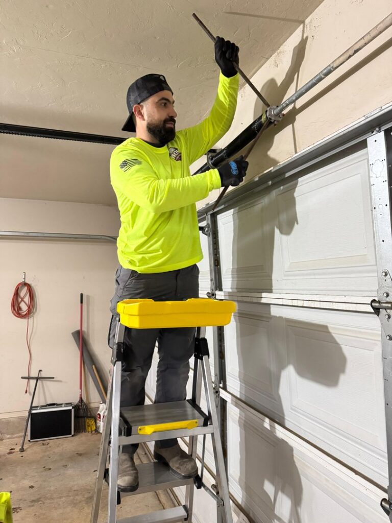 A garage door technician adjusting a torsion spring on a ladder for 405 Garage Pros in Edmond, OK.