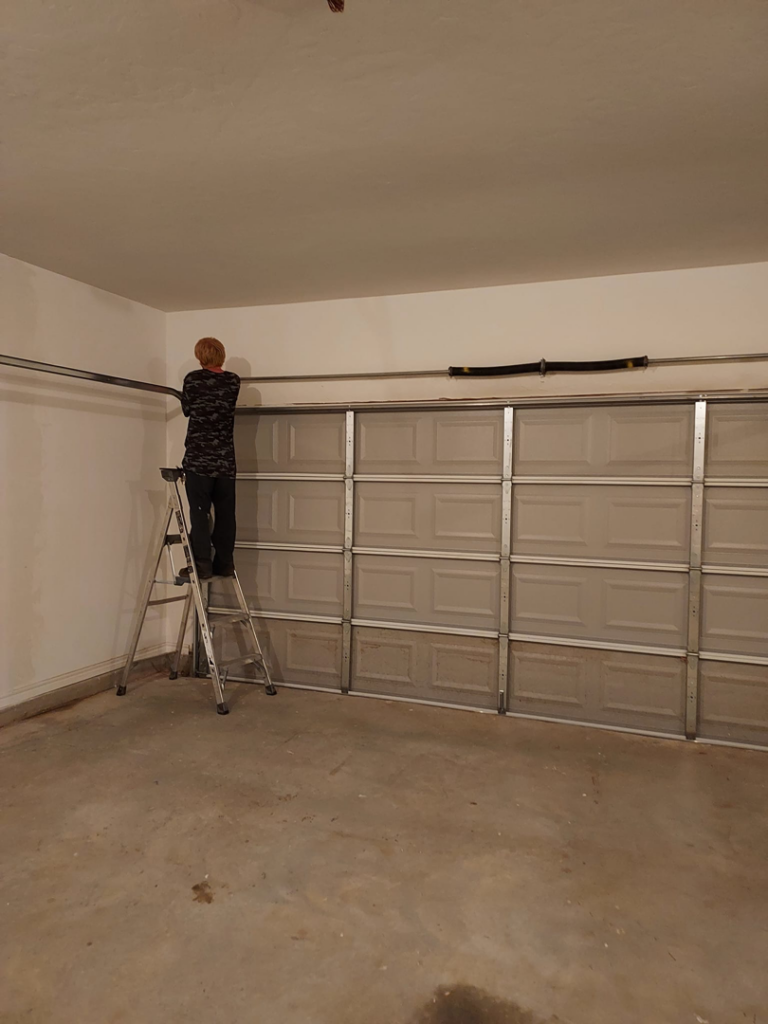 A garage door technician repairing a spring and track system at Zee's Garage Doors in Oklahoma City, OK.
