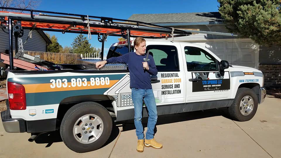 A garage door technician standing next to a branded service truck for 170 Springs LLC Garage Doors in Aurora, CO