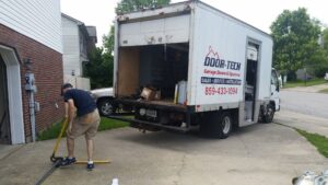 A Door-Tech LLC technician working on a garage door track with a branded service truck nearby in Lexington, KY.