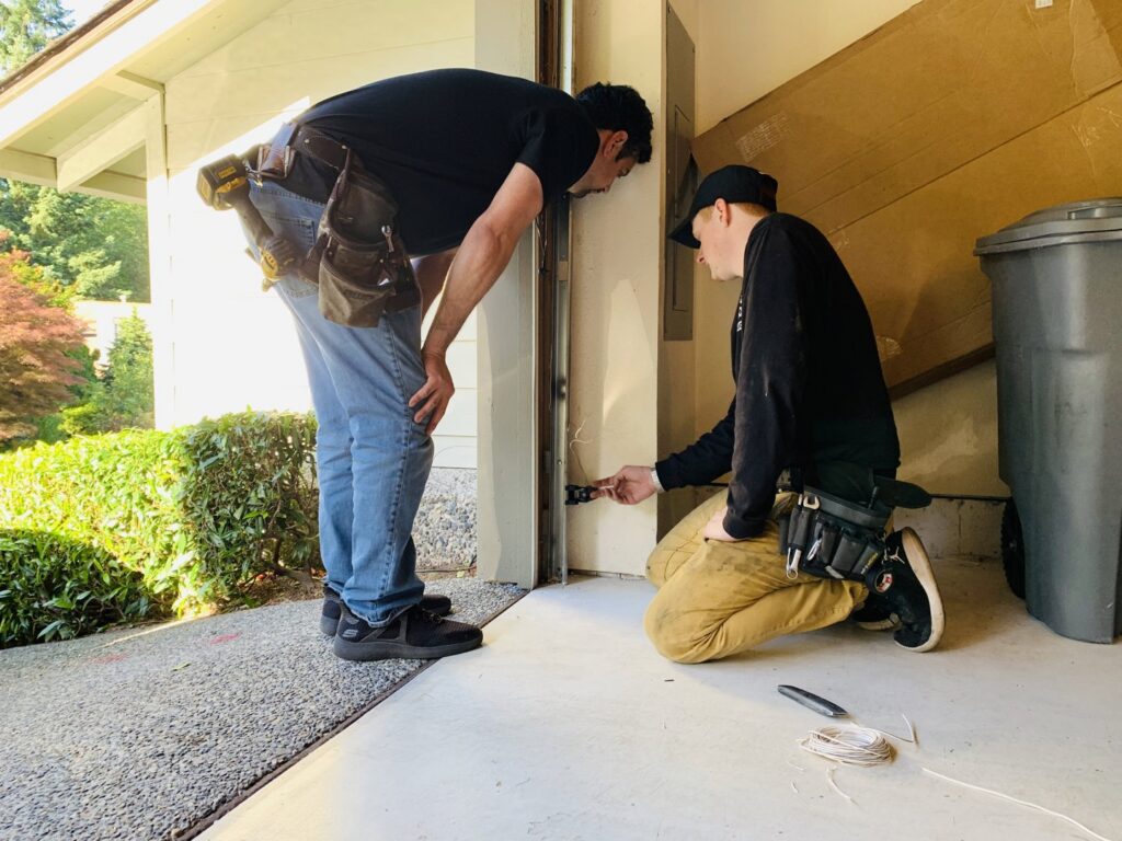 Two IGD Garage Door Repair technicians working on a garage door sensor, performing a repair or adjustment in Renton, WA.