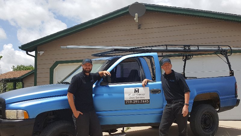 Two Million Garage Door Services technicians standing by their blue service truck, ready for jobs in Colorado Springs, CO.