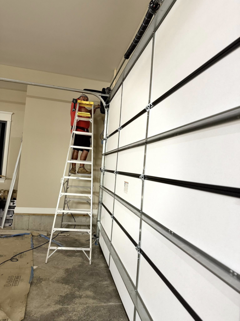 A technician on a ladder servicing a white garage door's track and opener system for Guest Garage Door Company in Lexington, KY.